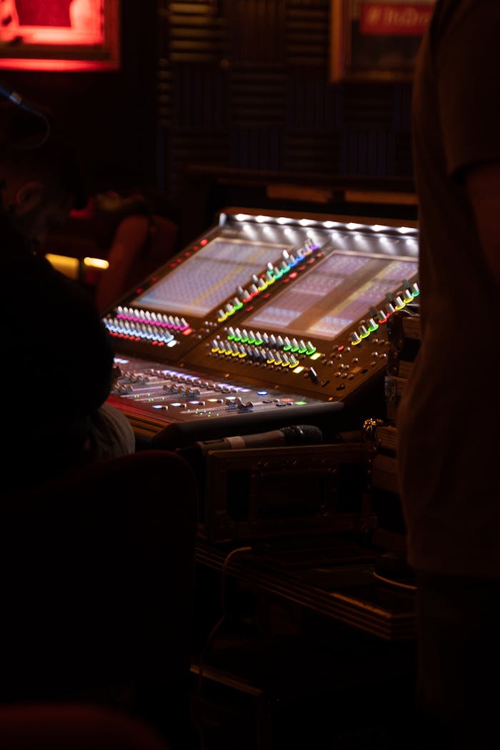 A professional sound mixer with colorful lights and audio equipment in a dark recording studio.
