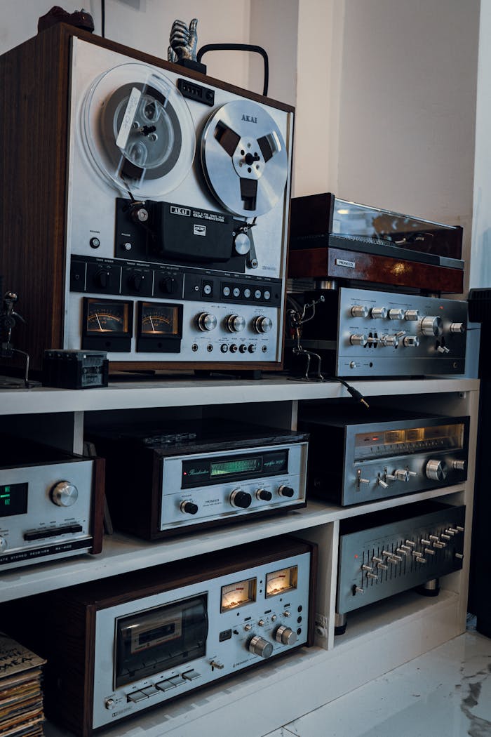 ours-journey A collection of vintage audio equipment including tape recorders and amplifiers on a white shelf indoors.
